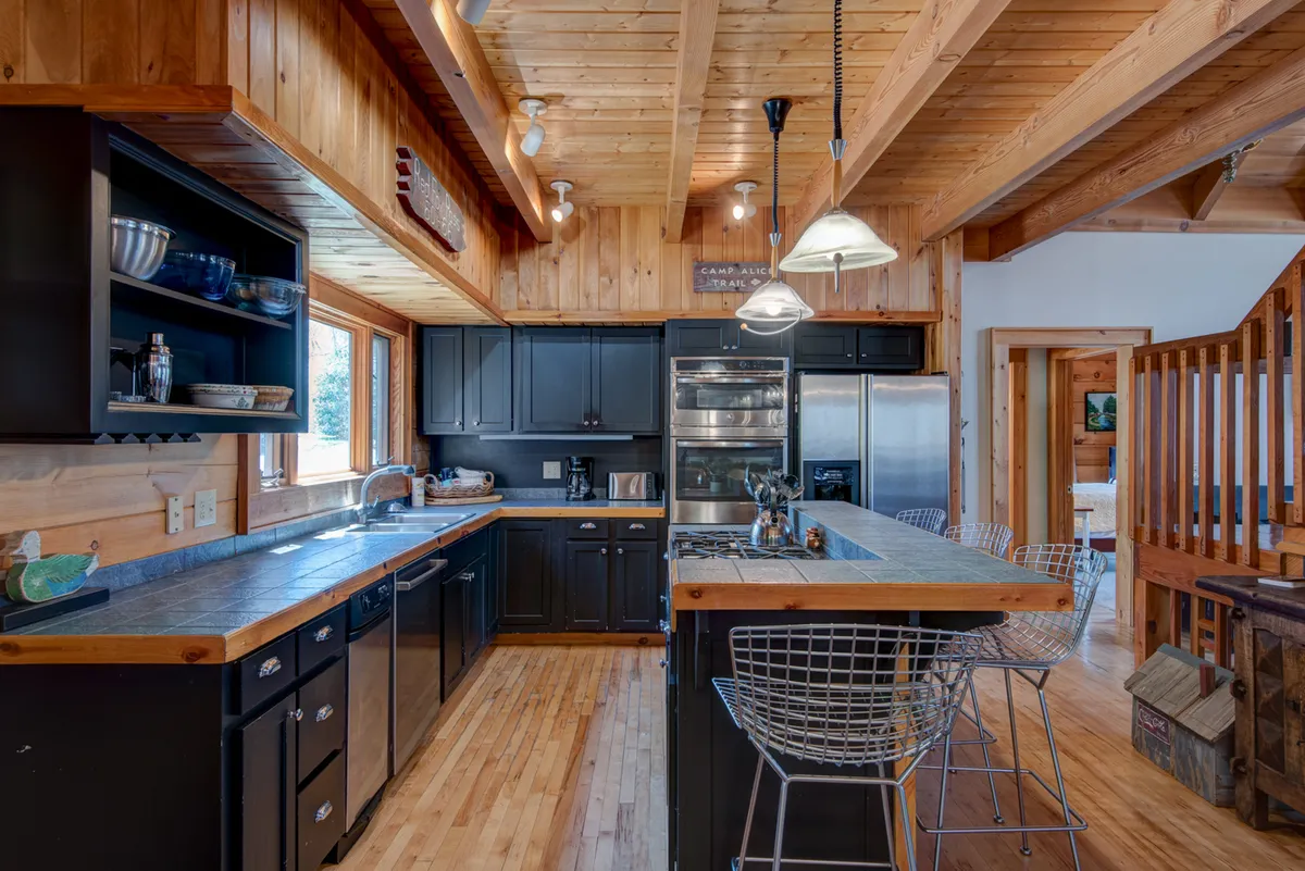 The image displays a spacious, upscale kitchen featuring a central island, stainless steel appliances, and wooden accents. It's a warm, welcoming setting perfect for preparing and sharing gourmet meals as described in the section.