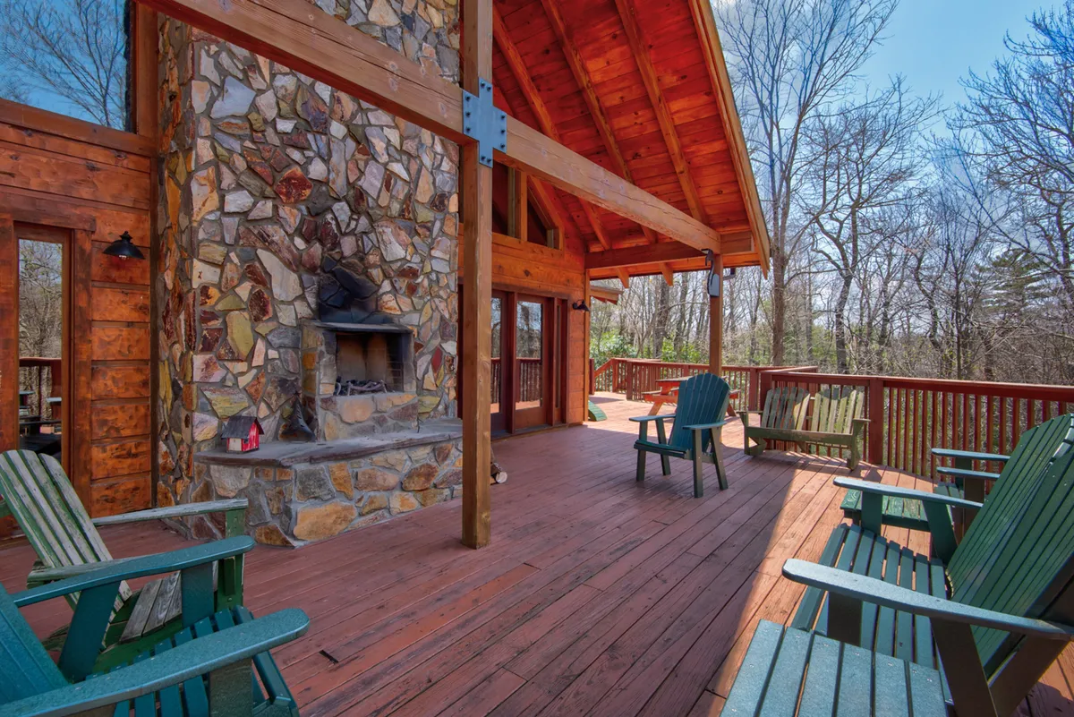 An inviting deck area with sturdy wooden beams and a stone fireplace, complete with cozy outdoor furniture. The view suggests an ideal spot for relaxing after a day of adventure, stargazing at night, or gathering with friends to share stories.