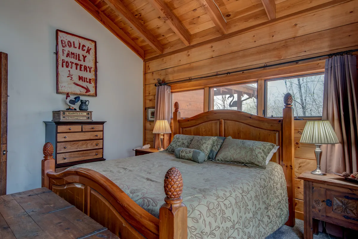 A cozy bedroom with a wooden bed, decorative pillows, a chest of drawers, warm lighting from bedside lamps, and a vintage sign on the wall. The room exudes warmth and comfort, perfect for unwinding after a long day.