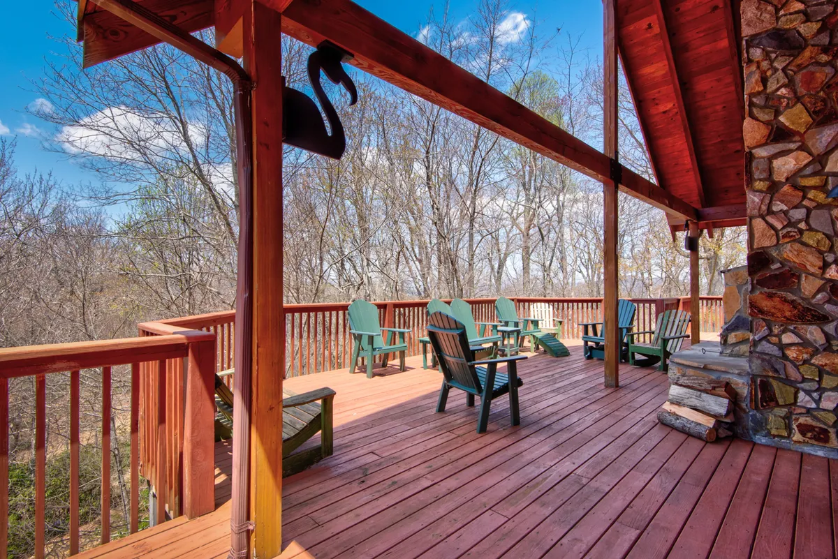 This scene showcases a spacious wooden deck with Adirondack chairs, a striking stone fireplace, and decorative touches. The setting is ideal for socializing, enjoying drinks by the fire, or soaking in the sunset views with friends or loved ones.