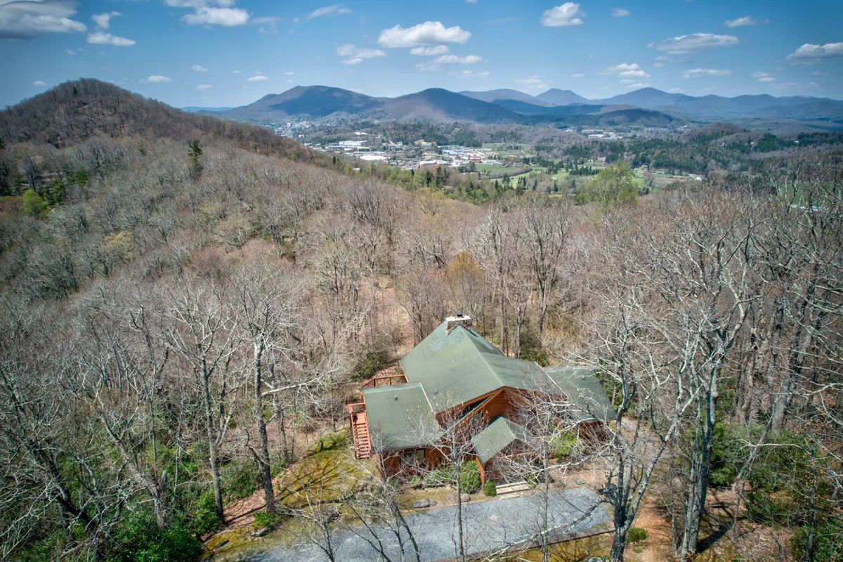 A classic log cabin is nestled amidst rolling mountains and lush forest, under a clear blue sky. The image captures the lodge’s natural setting, emphasizing its proximity to mountain adventures and local attractions. The surroundings evoke a sense of tranquility and the promise of outdoor exploration.