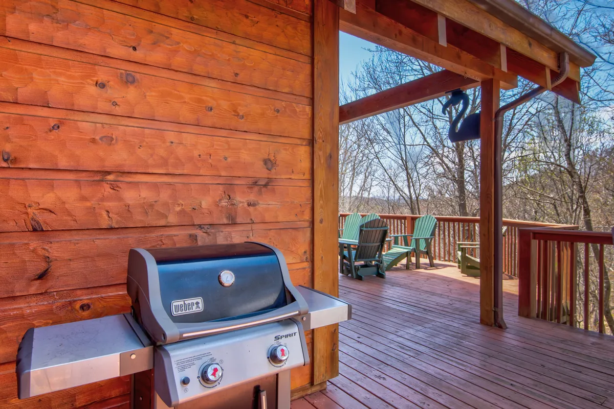 A view of the deck with a modern gas grill and comfortable seating. The grill is ready for barbecuing, with chairs nearby for guests to relax and socialize while taking in the natural surroundings.